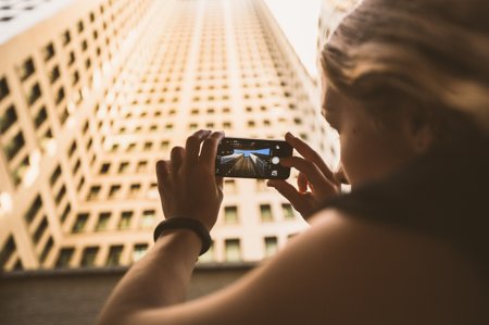 Frau fotografiert Hochhaus mit Smartphone